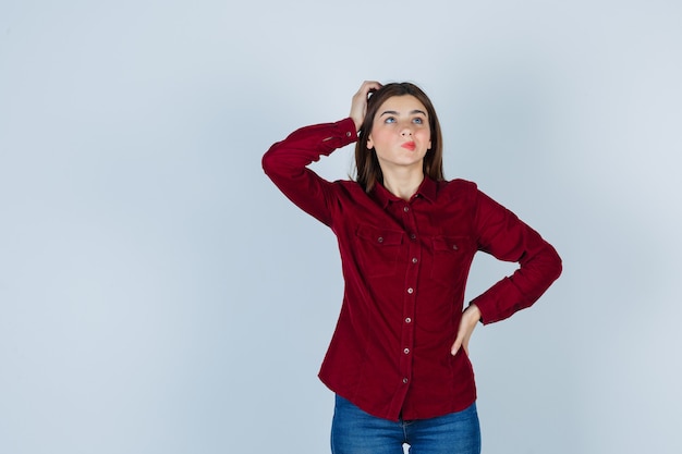 Girl in burgundy blouse standing in thinking pose and looking thoughtful