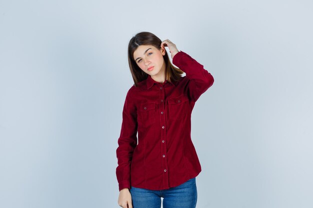 girl in burgundy shirt holding hand behind ear and looking curious.