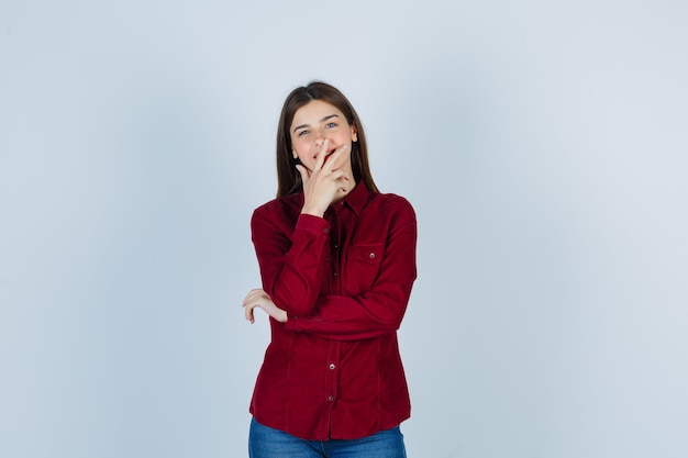 Free photo girl in burgundy shirt holding hand on mouth and looking cheery.