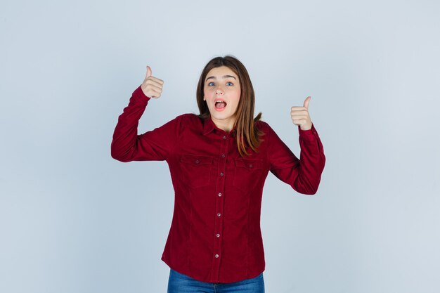 Free photo girl in burgundy shirt showing double thumbs up and looking amazed