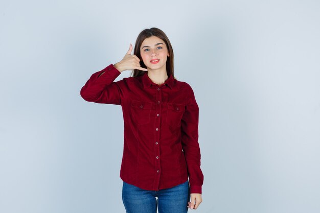 girl in burgundy shirt showing phone gesture and looking cheerful.