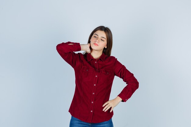 girl in burgundy shirt suffering from neck pain and looking tired.