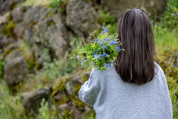 少女は春の森で集めた花束を背負って後ろから眺める