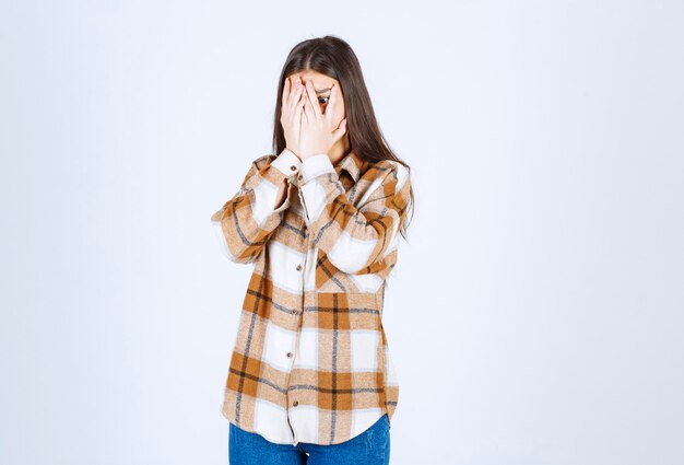  girl in casual clothes covering her full face on white wall. 