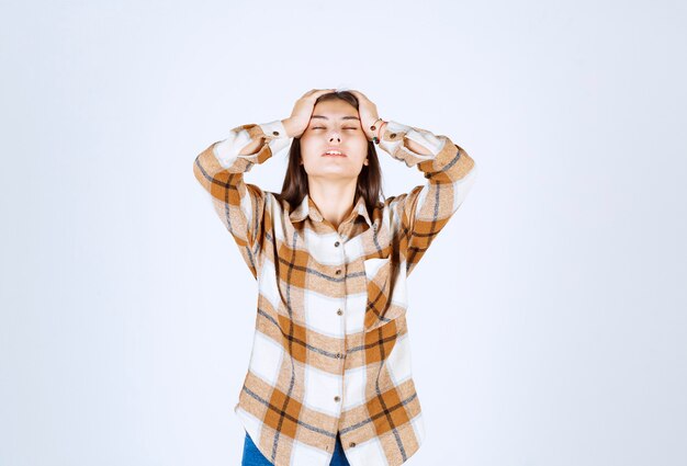  girl in casual clothes giving holding her head on white wall. 