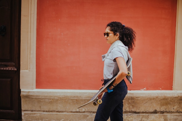 Girl in casual outfit holding skateboard walking