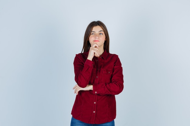 girl in casual shirt keeping finger on chin, looking away and looking thoughtful