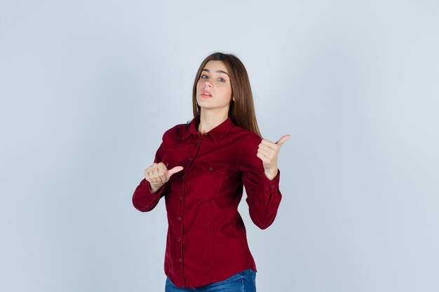 girl in casual shirt pointing right with thumbs and looking curious 