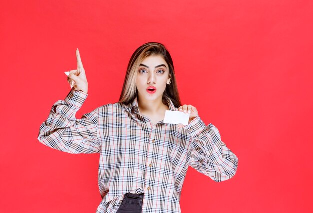 Girl in checked shirt holding a business card and looks surprized