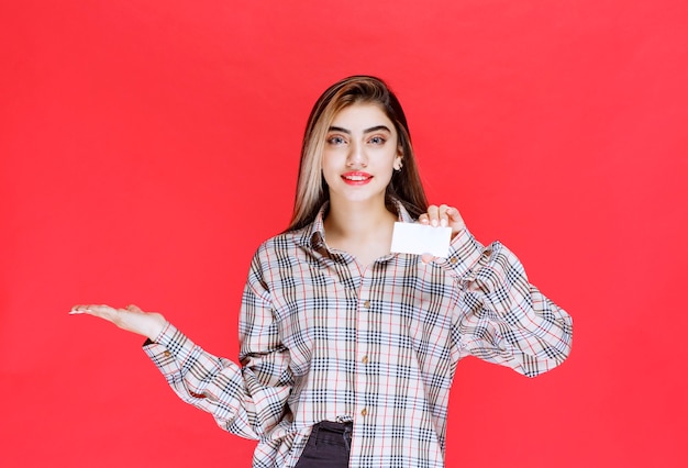 Girl in checked shirt holding a business card and pointing at her colleague