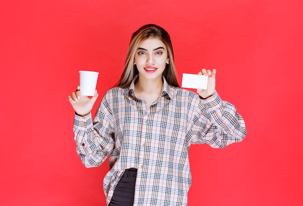 Girl in checked shirt holding a coffee cup and presenting her business card