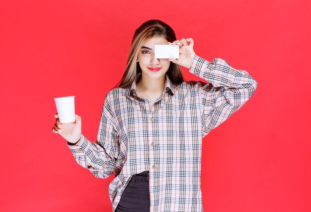 Girl in checked shirt holding a coffee cup and presenting her business card