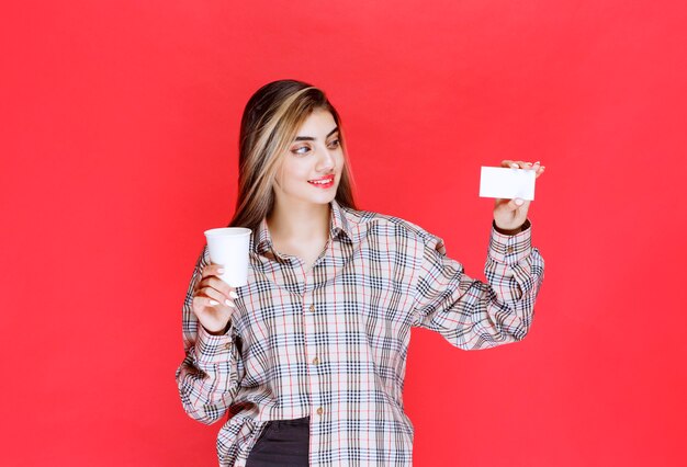 Girl in checked shirt holding a coffee cup and presenting her business card