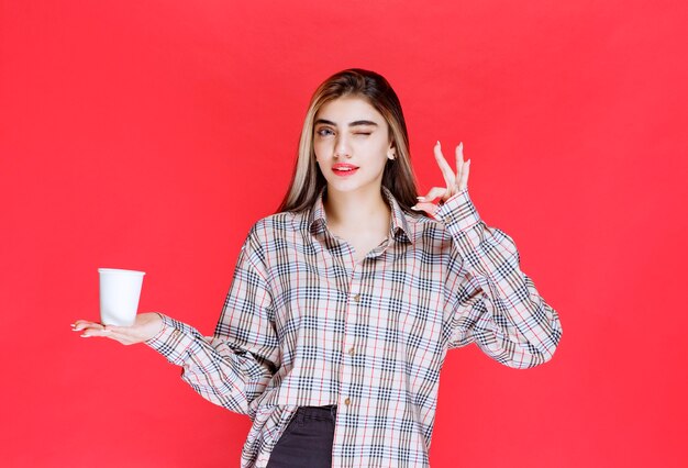 Girl in checked shirt holding a white disposable coffee cup and enjoying the taste