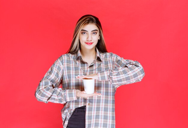 Girl in checked shirt holding a white disposable coffee cup 