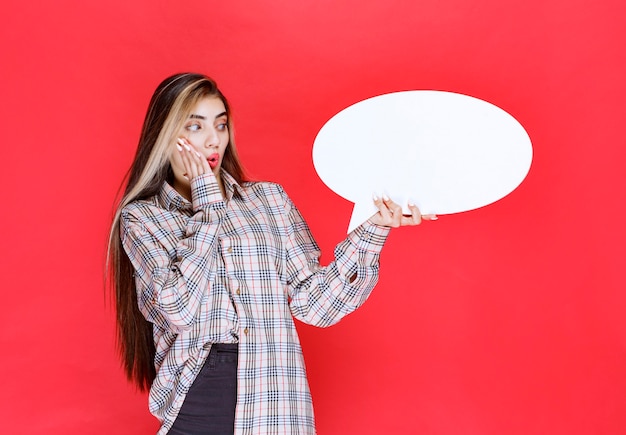 Girl in checked sweater holding an ovale ideaboard looks confused and excited