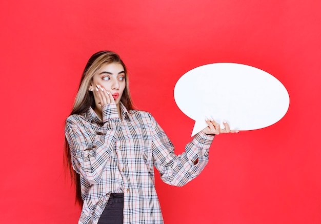 Girl in checked sweater holding an ovale ideaboard looks confused and excited