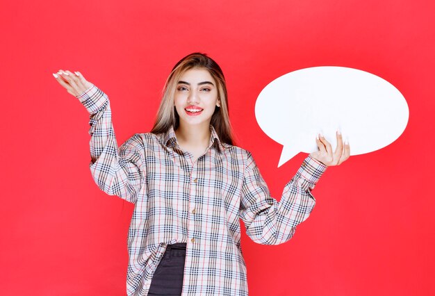 Girl in checked sweater holding an ovale ideaboard and pointing at the participants