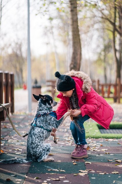 Girl child playing with dog in autumn sunny park