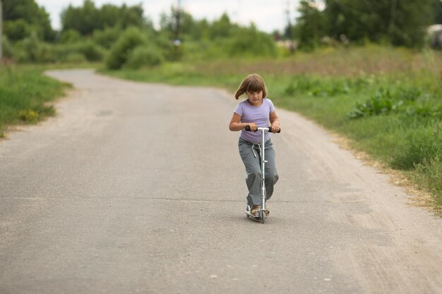 Girl child riding scooter on the road In the countryside child safety childhood