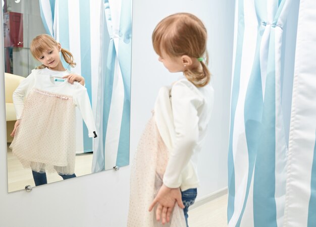 Девушка выбирает, примеряет платье в торговом центре, смотрит в зеркало.