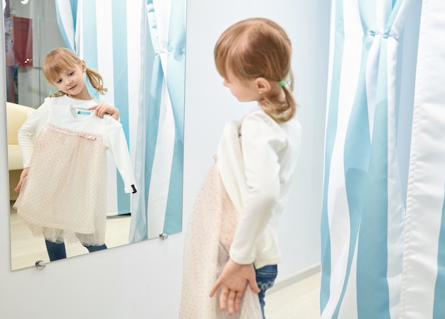 Girl choosing, trying dress on in mall, looking at mirror.