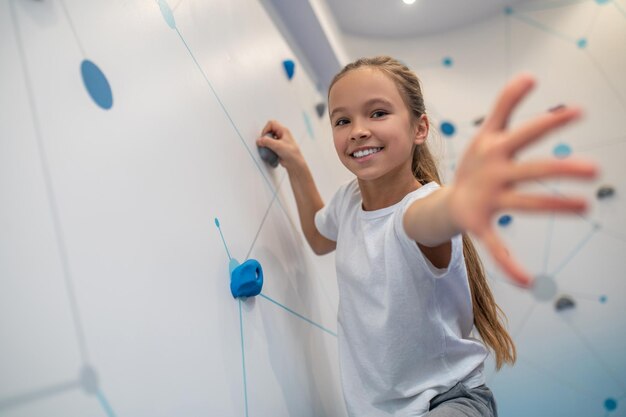 Girl climbing wall and reaching out to camera