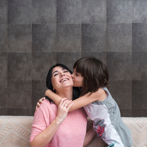 Girl on couch kissing mother on cheek