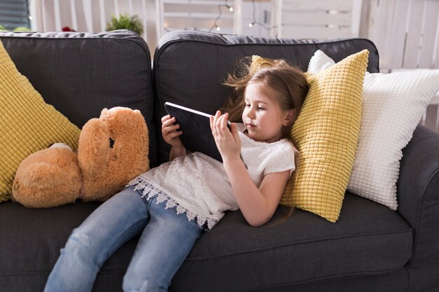 Girl on couch with tablet and teddy