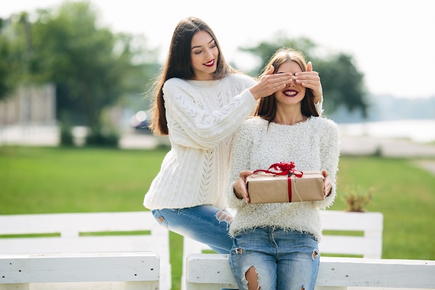 Girl covering her eyes with another girl with a gift in her lap