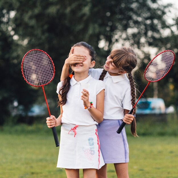 Girl covering her friend eyes holding badminton