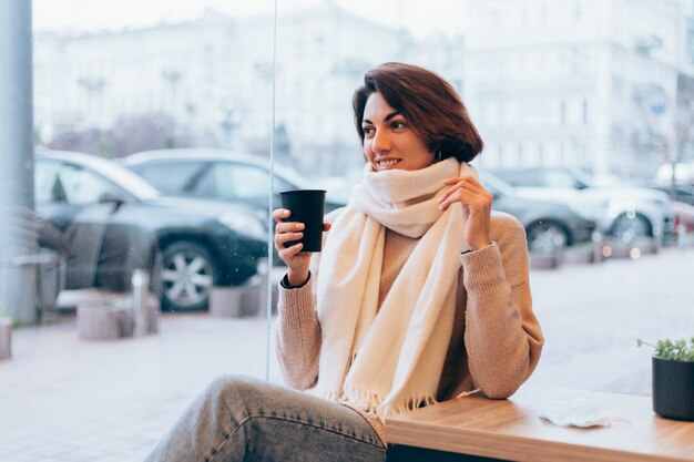 A girl in a cozy cafe warms herself up with a cup of hot coffee