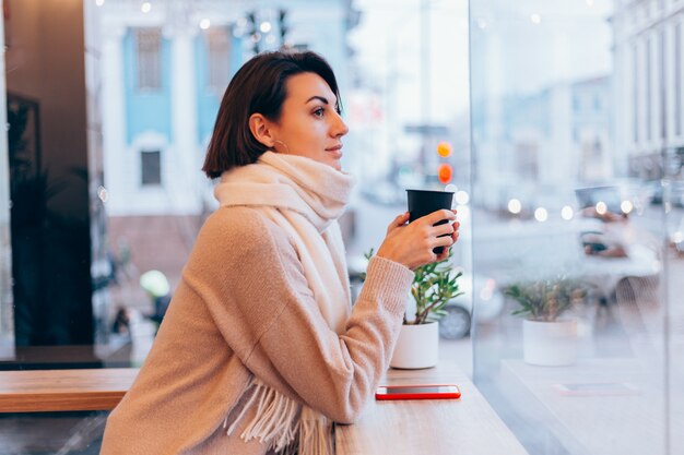 A girl in a cozy cafe warms herself up with a cup of hot coffee
