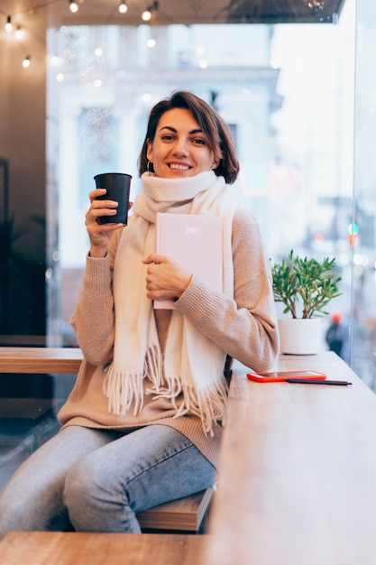 A girl in a cozy cafe warms herself up with a cup of hot coffee