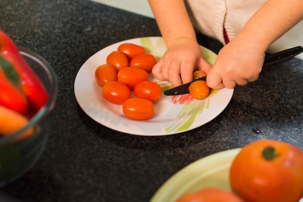 Pomodori di taglio ragazza sul piatto sopra il piano di lavoro della cucina