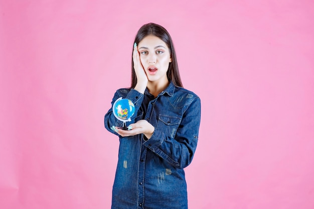 Free photo girl in denim jacket holding a globe and looks surprized