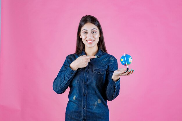 Girl in denim jacket holding a globe and pointing at it