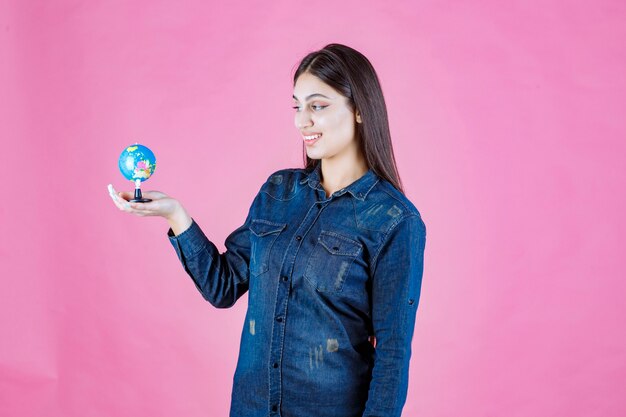 Girl in denim jacket holding a mini globe inside her palm