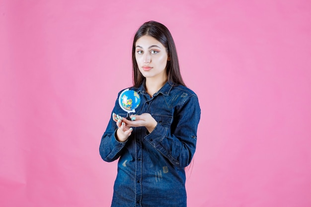 Girl in denim jacket holding a mini globe inside her palm