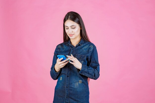 Девушка в джинсовой рубашке болтает на своем смартфоне