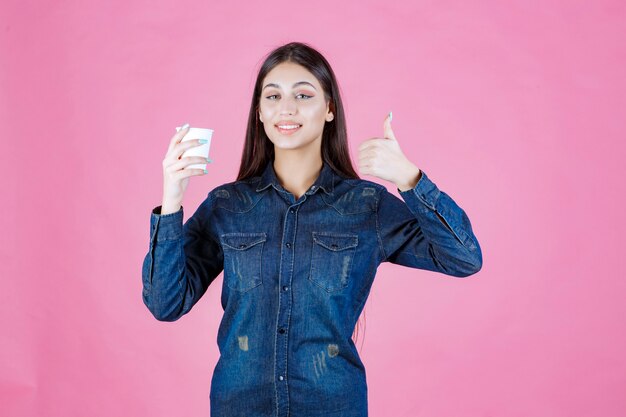 Girl in denim shirt having coffee and doing thumb up