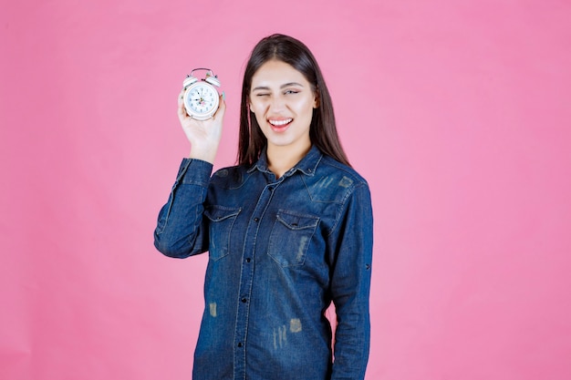 Girl in denim shirt holding an alarm clock and promoting it