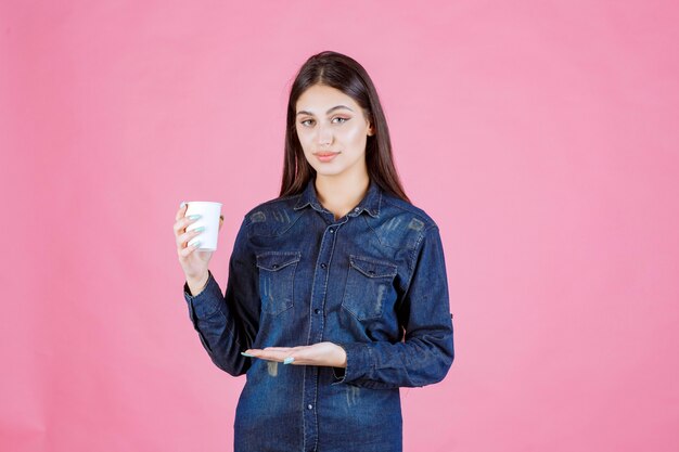 Девушка в джинсовой рубашке держит чашку кофе и чувствует себя уверенно