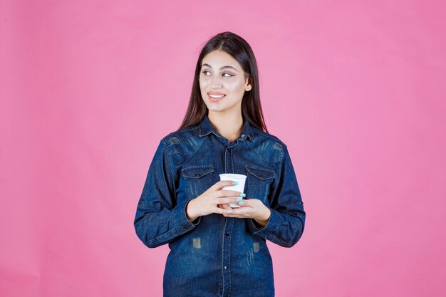 Девушка в джинсовой рубашке держит чашку кофе и чувствует себя уверенно