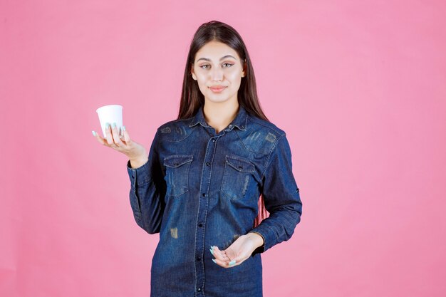 Ragazza in camicia di jeans che tiene una tazza di caffè e si sente positiva