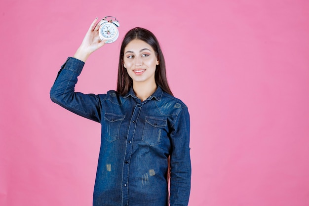 Girl in denim shirt holding and promoting an alarm clock