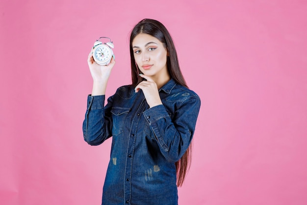 Girl in denim shirt holding and promoting an alarm clock