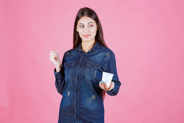 Girl in denim shirt offering a cup of coffee to her friend