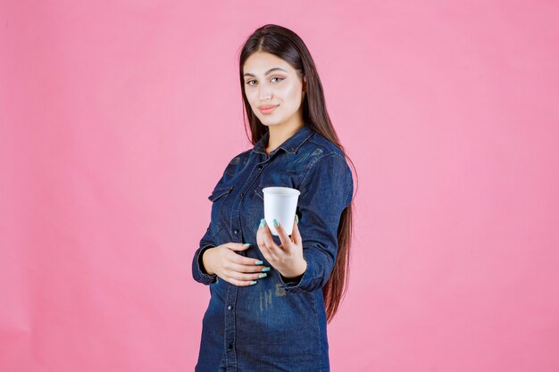 Girl in denim shirt offering a cup of coffee to her friend