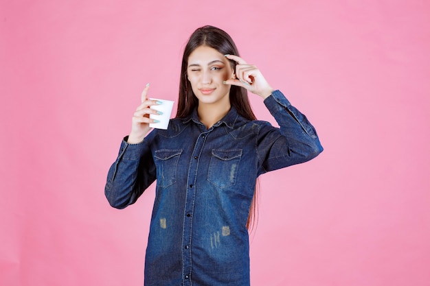 Girl in denim shirt showing the amount of coffee in the cup